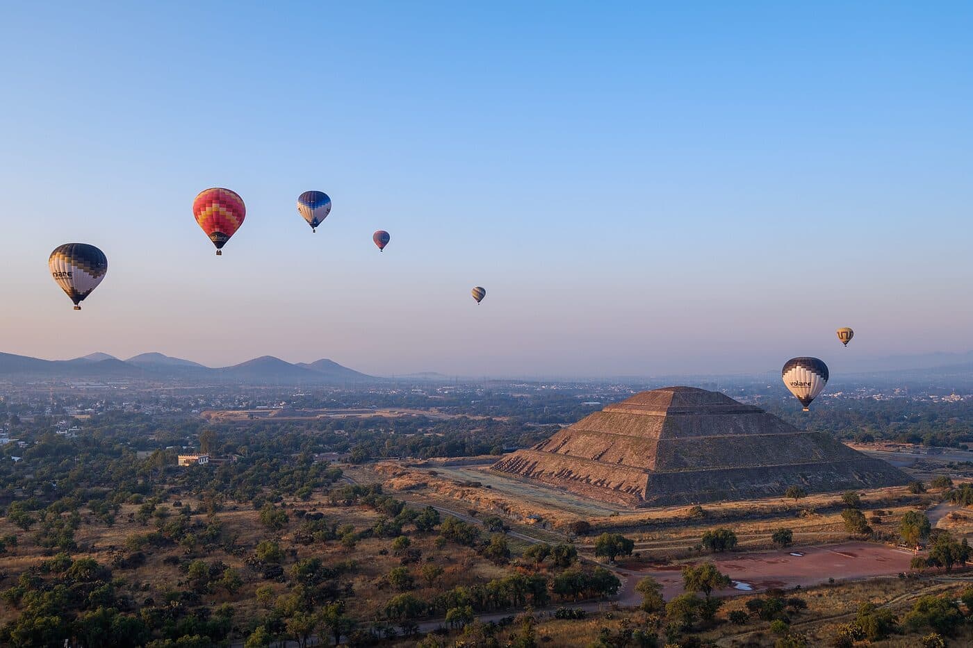 Hot air balloons drifting over a stepped pyramid at dawn