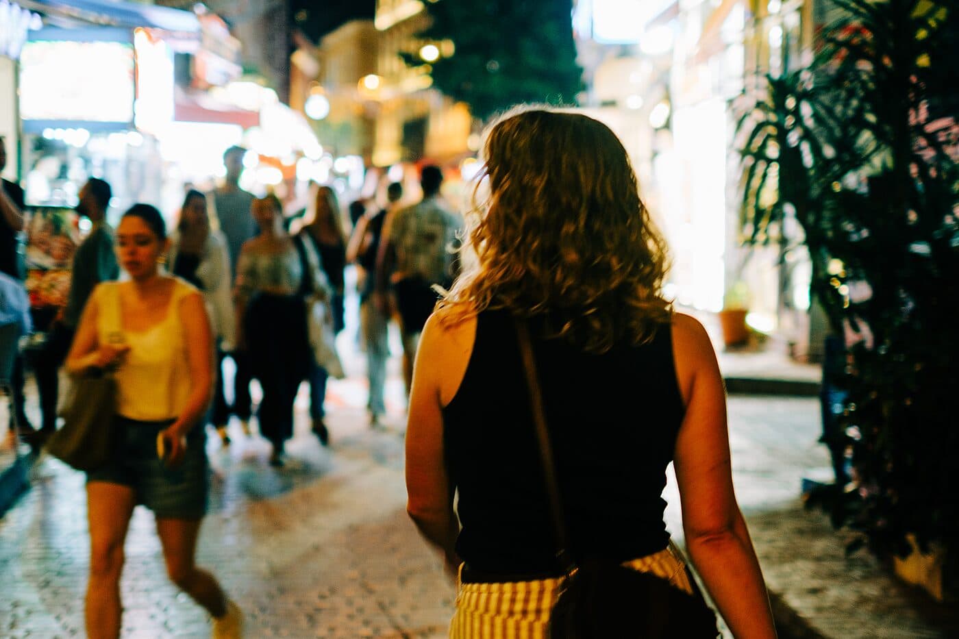 A woman walking a crowded street under strung lights at night