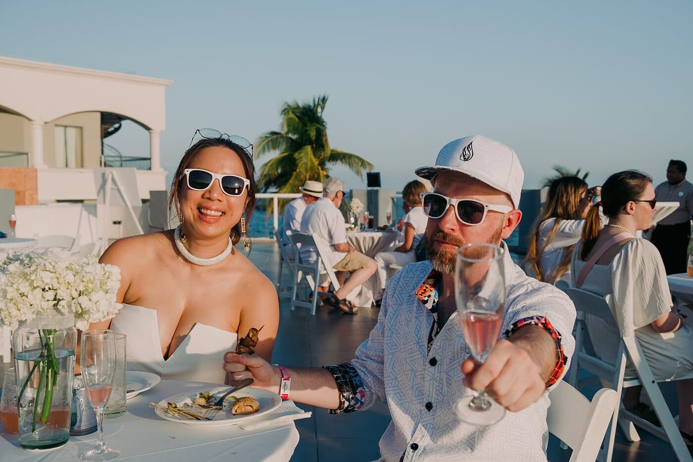 Two people raising a glass at an outdoor table by the sea