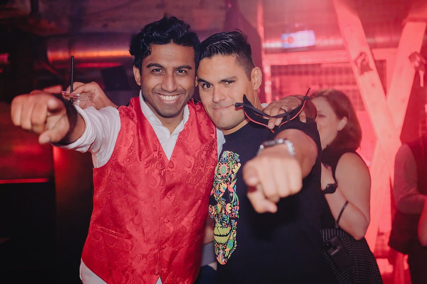 Two people pointing at the camera in a red-lit room